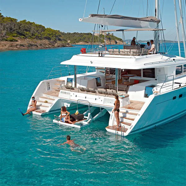 Guests swimming and sunning off the transom steps of a catamaran anchored in turquoise water